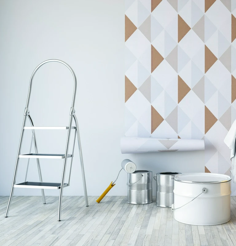 Metalowa drabina, puszki z&nbsp;farbą i&nbsp;wałek na&nbsp;tle ściany, która jest w&nbsp;trakcie tapetowania
