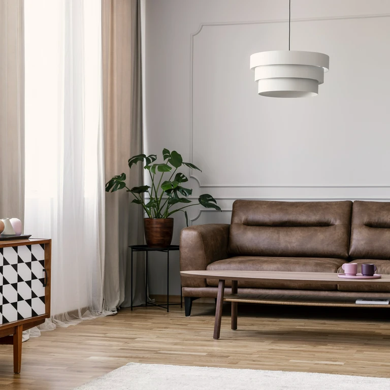 Nowoczesny salon z&nbsp;brązową skórzaną sofą, designerską lampą i&nbsp;stolikiem kawowym na&nbsp;tle jasnych ścian