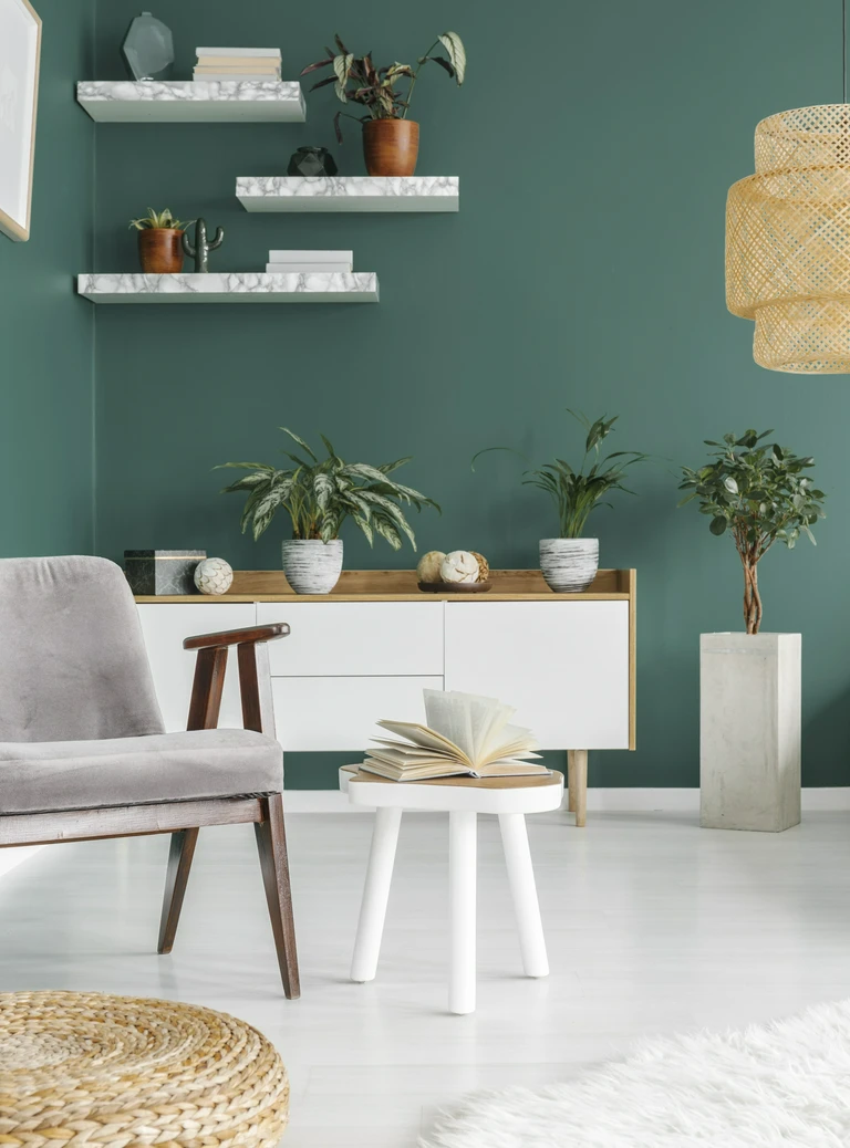 Stylowy kącik z&nbsp;zieloną ścianą, białą komodą, roślinami doniczkowymi i&nbsp;marmurowymi półkami